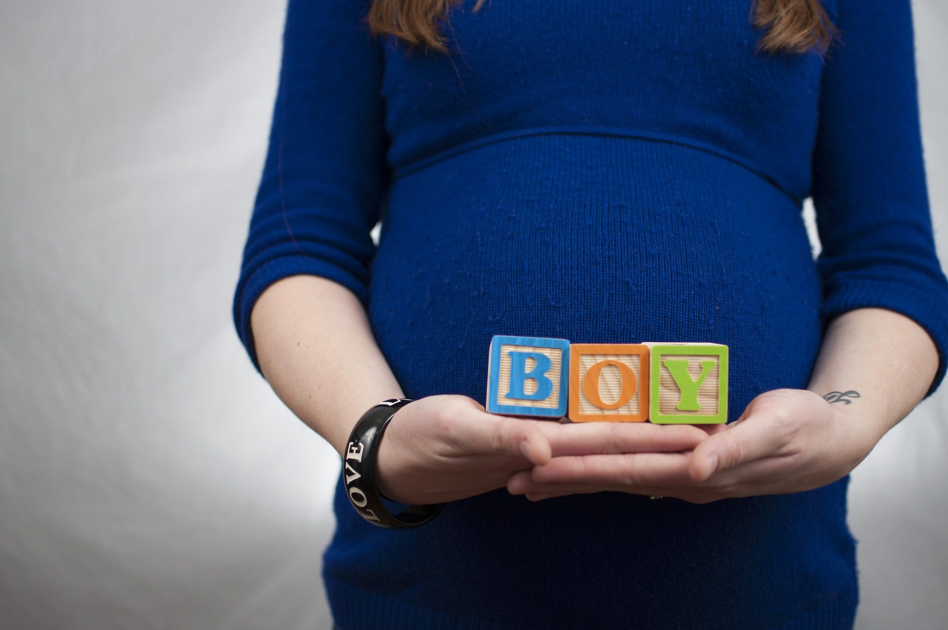 Woman in a blue shirt, holding blocks that say "boy" in front of her pregnant belly.