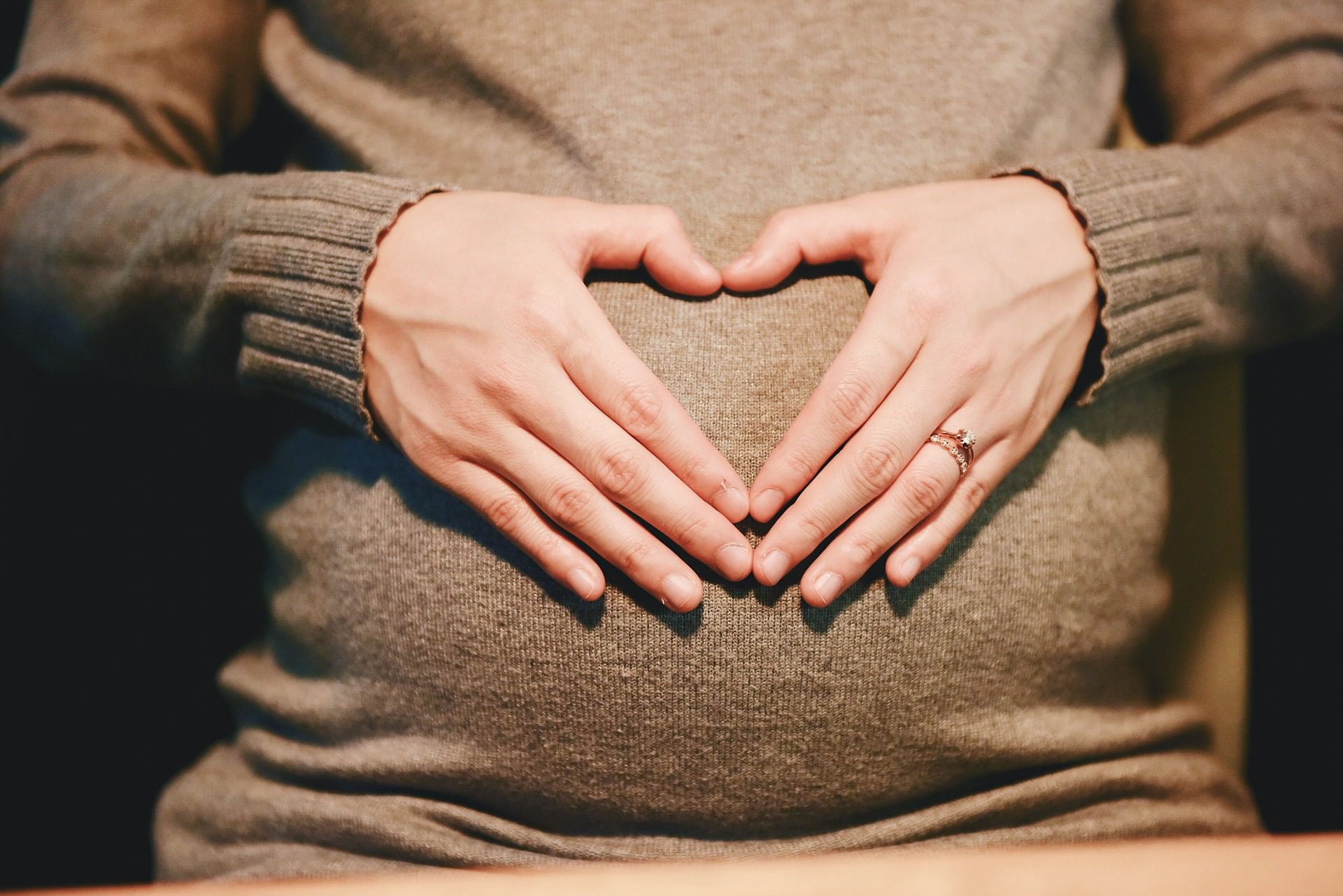 Woman holding her hands in a heart shape over her pregnant belly.